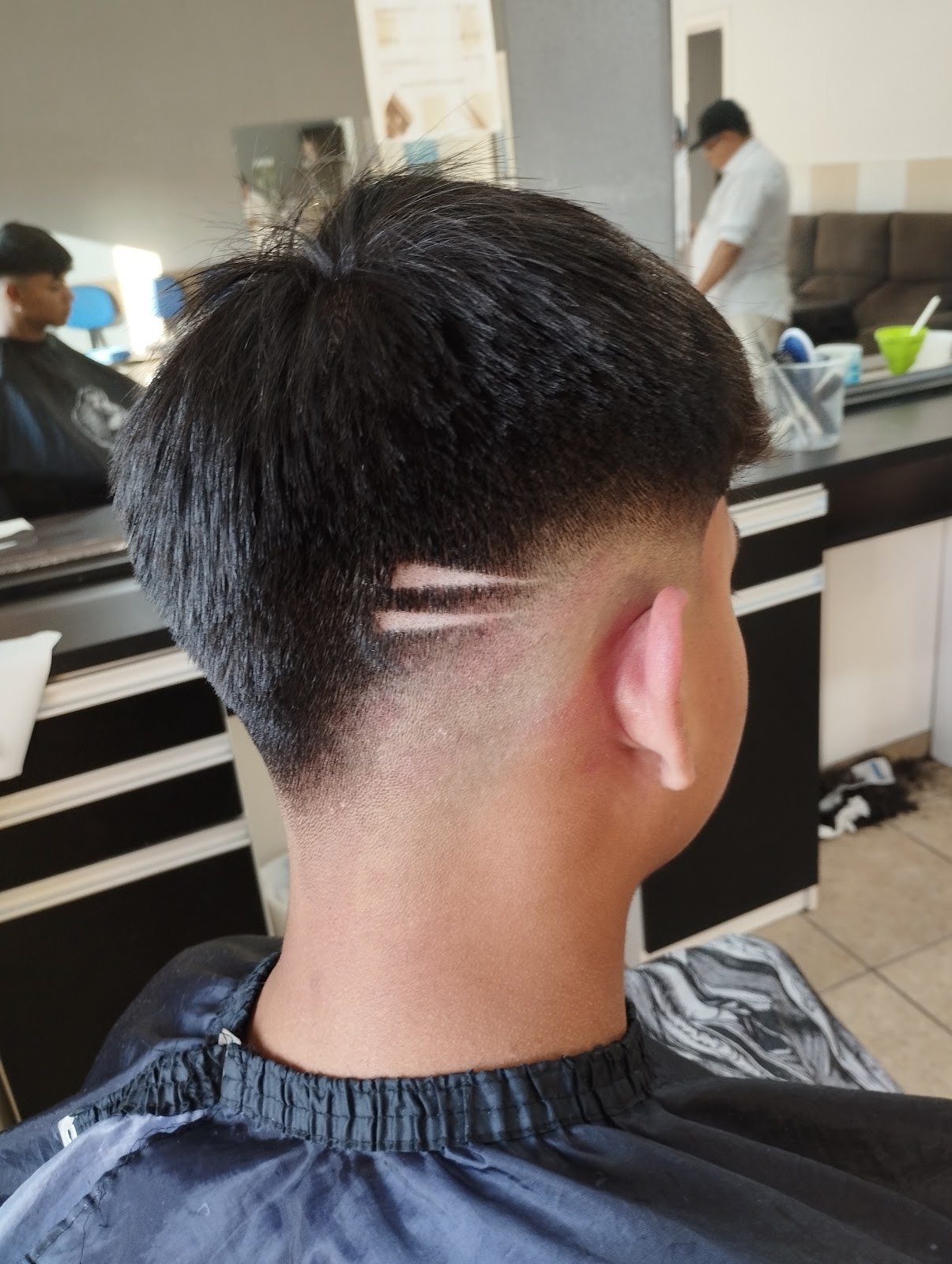 Barbeiro cortando o cabelo de um cliente em frente ao espelho na Barbearia Guih Santos